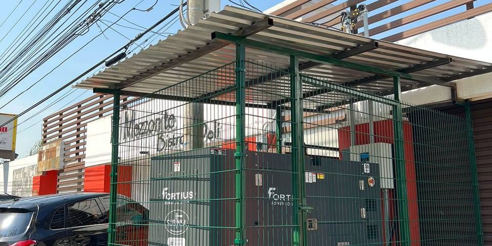 Generador eléctrico Fortius dentro de una estructura protectora hecha a base de varandales de hierro y un techo de lámina. Equipo se encuentra al frente de un restaurante llamado Mezzonite Deli & Bistro.