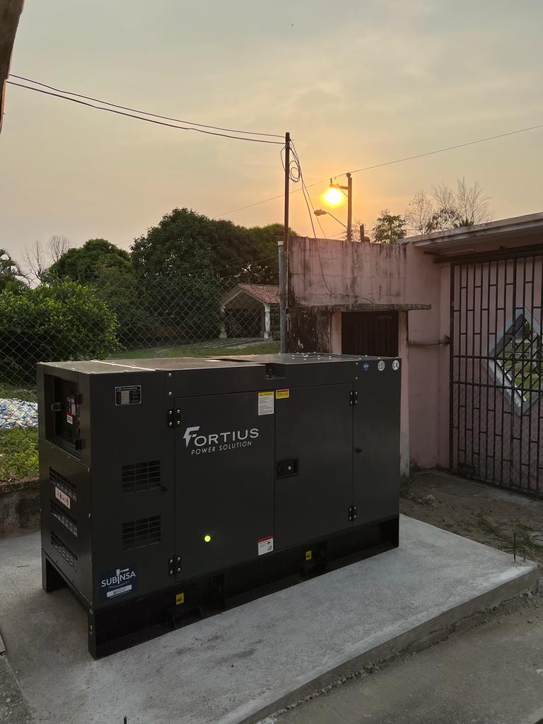 Generador eléctrico Fortius sobre una plancha de cemento. Al lado derecho al fondo se logra ver un muro rosado que pertenece a la casa en donde está ubicado el equipo.
